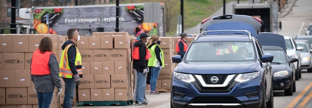 Volunteers organize boxed food supplies beside cars at a distribution site